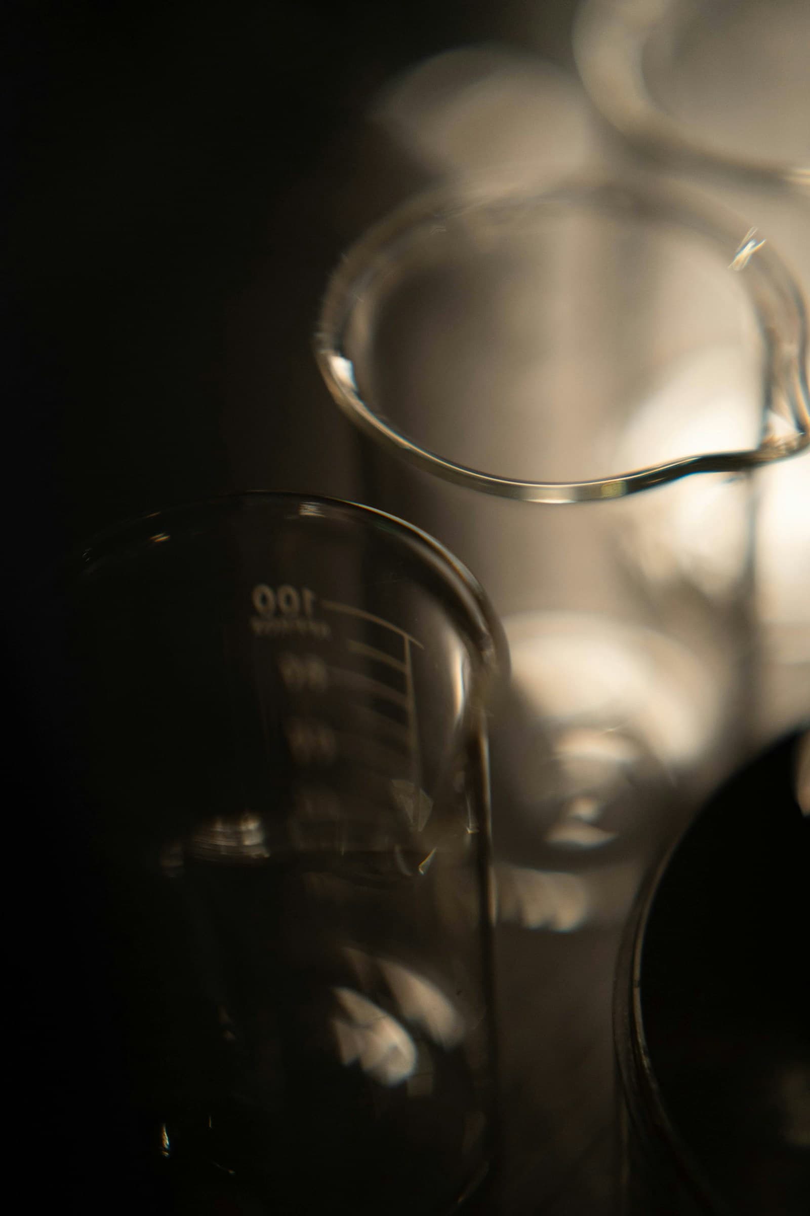 Clean unbranded laboratory beakers in side-lit moody studio composition — representative of the analytical rigour Pepoderma applies to every cosmetic-grade peptide active before release.